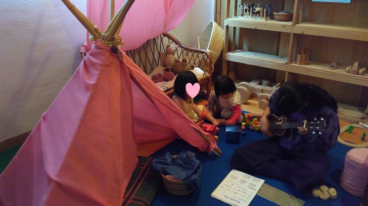一緒に遊ぶ幼い女の子二人とウクレレを練習する少女